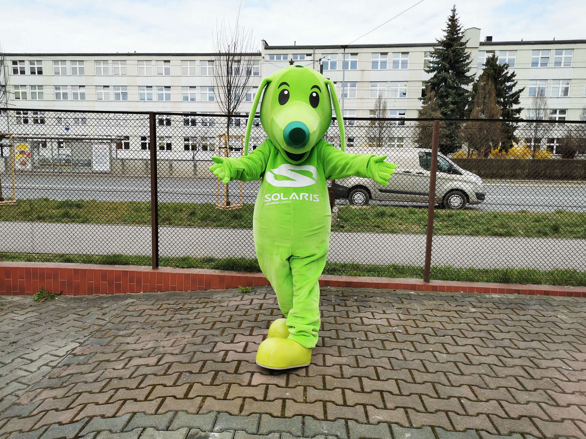 Na fotografii widnieje strój reklamowy w postaci psa jamnika pozujący do zdjęcia przed siedzibą firmy Elabika